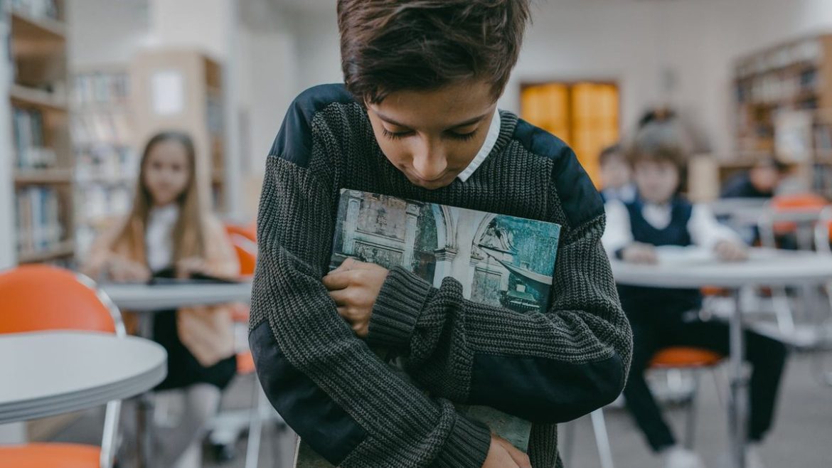 Хлопчик стоїть осторонь у шкільній бібліотеці