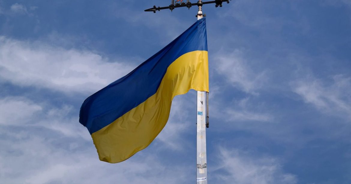 Державний прапор України на флагштоку на тлі неба з хмарами